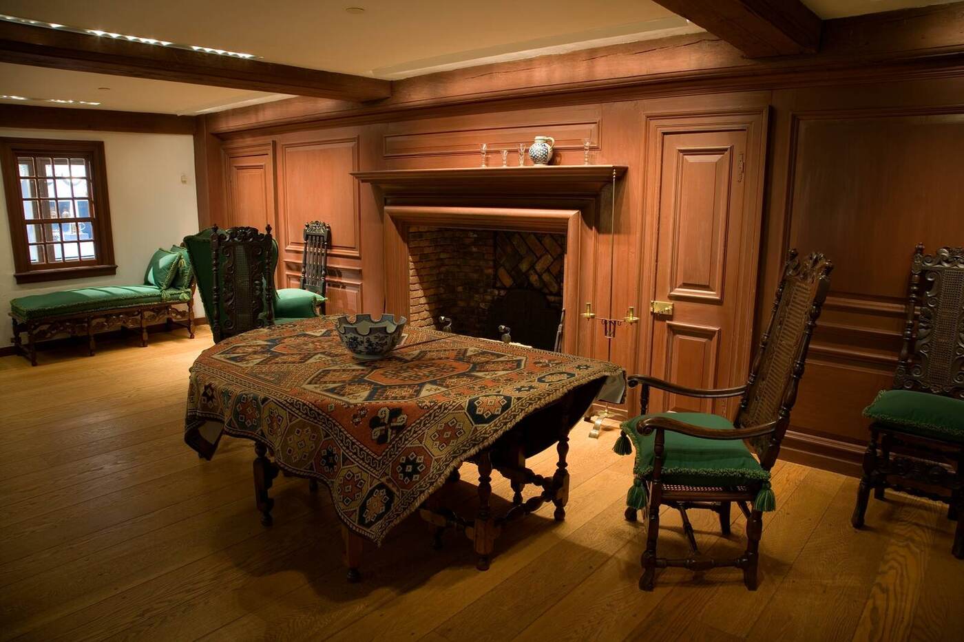 A colonial paneled room with a carpet-draped table, rush chairs, and wide pine floors